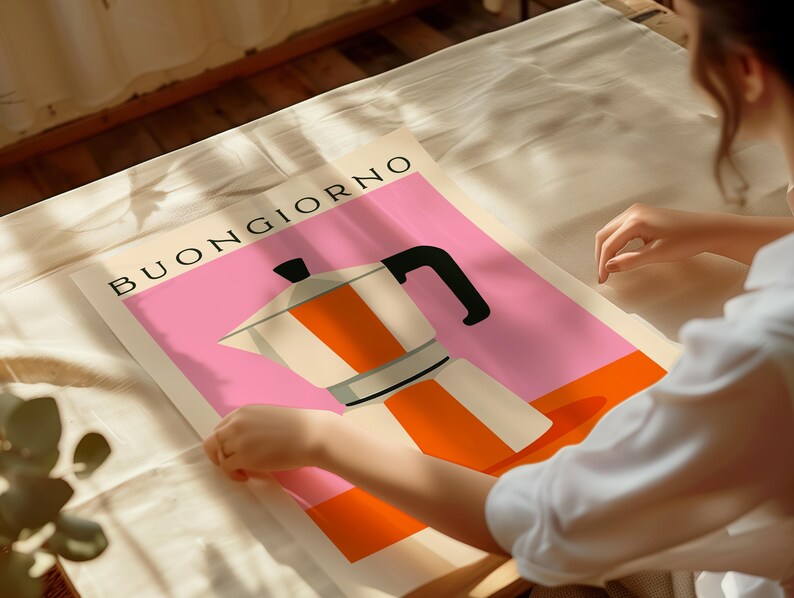 Puede incluir: Un p&oacute;ster con una ilustraci&oacute;n estilizada de una cafetera italiana en naranja, blanco y negro sobre un fondo rosa y naranja. La palabra "BUONGIORNO" est&aacute; impresa en negro en la parte superior. Una persona sostiene el p&oacute;ster.