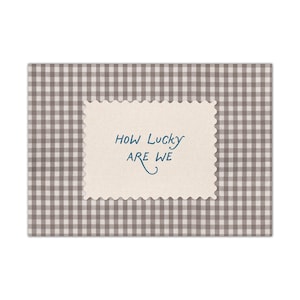 K&ouml;nnte beinhalten: Eine Gru&szlig;karte mit beigefarbenem, gezacktem Rand, die den Text "HOW LUCKY ARE WE" in blauer Schrift tr&auml;gt. Die Karte ist vor einem grau-wei&szlig; karierten Hintergrund platziert, was ein schlichtes und elegantes Design ergibt.