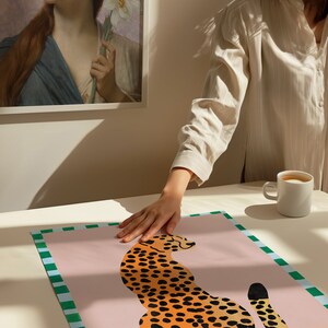 May include: A pink and green patterned poster with a stylized illustration of a cheetah in orange and black. The cheetah is sitting with its tail curled around its body.