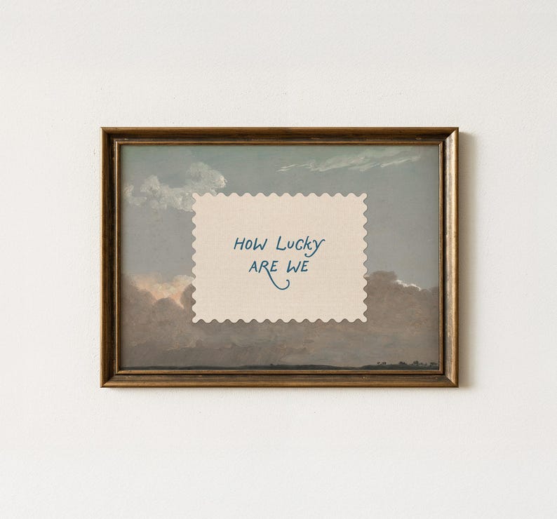 K&ouml;nnte beinhalten: Gerahmtes Kunstwerk mit einer Landschaftsmalerei mit bew&ouml;lktem Himmel. Ein cremefarbenes Papier mit gezackten Kanten und dem Text "HOW LUCKY ARE WE" ist auf das Gem&auml;lde gelegt. Der Rahmen ist dunkel und aufwendig goldfarben.