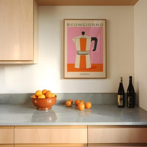 Puede incluir: Una escena de cocina con un p&oacute;ster enmarcado con la palabra "Buongiorno" y una ilustraci&oacute;n de una cafetera espresso. Un cuenco de terracota con naranjas est&aacute; sobre una encimera. Dos botellas de vino est&aacute;n a la derecha.