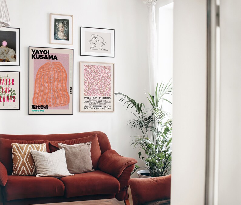 Puede incluir: Un interior de sala de estar con un sof&aacute; rojo y varios carteles enmarcados en la pared. Los carteles muestran obras de arte de Yayoi Kusama y William Morris. Una planta en maceta se encuentra en el suelo junto al sof&aacute;.