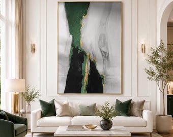 May include: A large vertical abstract painting featuring bold strokes of deep forest green, black, and white, accented with metallic gold leaf details. The artwork is framed in a thin gold border and displayed on a white wall above a sofa.