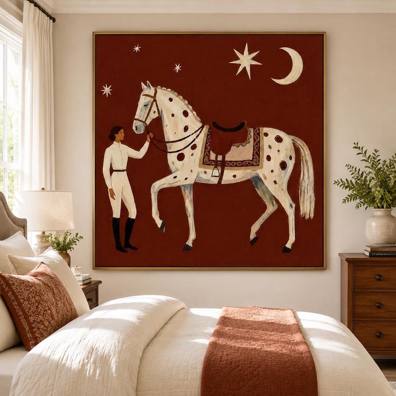 May include: A square wall art piece featuring a white spotted horse with a saddle and a person in white equestrian attire standing beside it. The background is a deep red color decorated with a white crescent moon and several white stars.