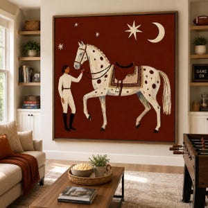 May include: A large square wall art piece featuring a white spotted horse with a brown saddle and a rider in white equestrian attire. The background is a deep rust red color decorated with a white crescent moon and several four-pointed stars.