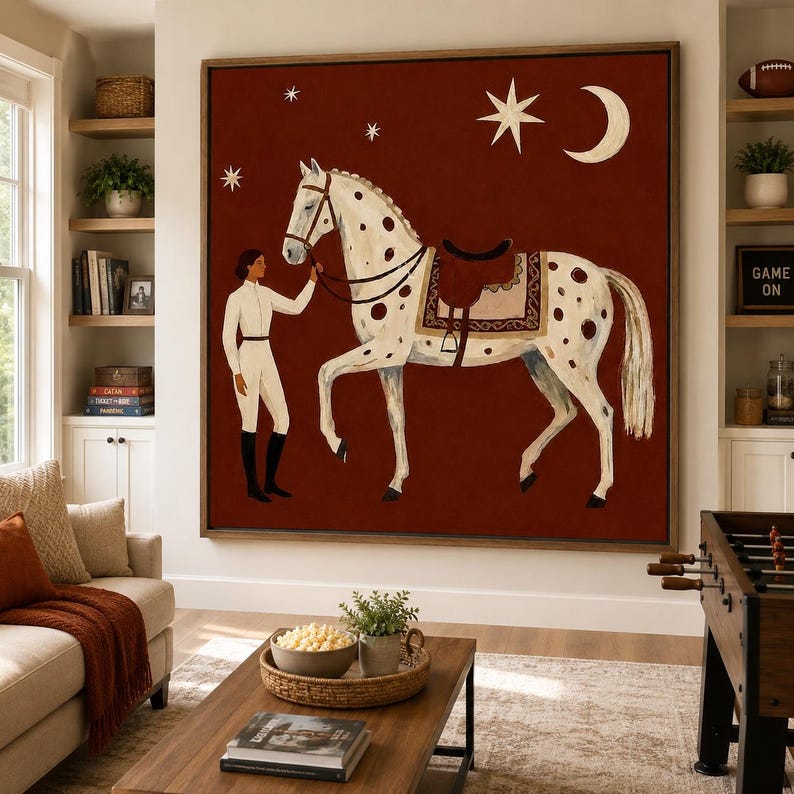 May include: A large square wall art piece featuring a white spotted horse with a brown saddle and a rider in white equestrian attire. The background is a deep rust red color decorated with a white crescent moon and several four-pointed stars.