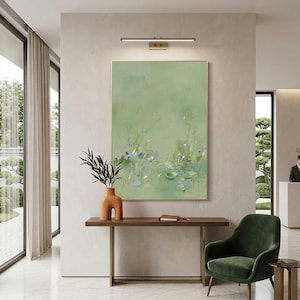 May include: A large framed abstract painting with a green background and floral details hangs on a wall. A wooden console table with a vase and a green velvet chair are in front of the painting. A small side table and a window are also visible.