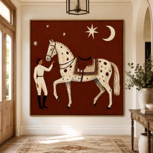 May include: A square wall art print featuring a person in white equestrian attire standing beside a white horse with brown spots. The horse wears a brown saddle. The background is a deep red color decorated with a white crescent moon and stars.