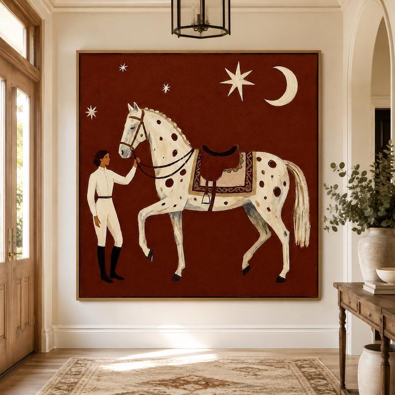 May include: A square wall art print featuring a person in white equestrian attire standing beside a white horse with brown spots. The horse wears a brown saddle. The background is a deep red color decorated with a white crescent moon and stars.