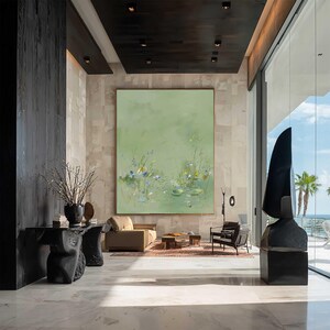 May include: A large, framed abstract painting with a light green background dominates a modern living space. The artwork features delicate floral and aquatic elements in shades of blue, yellow, and white. The room includes a sofa, chairs, and a sculpture.
