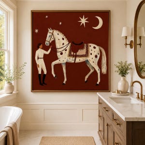 May include: A square framed painting on a dark red background featuring a person in white equestrian attire standing next to a white horse with brown spots. The horse wears a saddle and bridle. Above them are a white crescent moon and several stars.