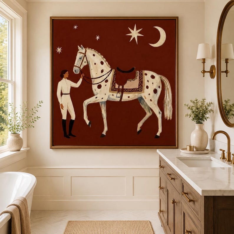 May include: A square framed painting on a dark red background featuring a person in white equestrian attire standing next to a white horse with brown spots. The horse wears a saddle and bridle. Above them are a white crescent moon and several stars.