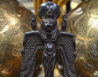 May include: A black wooden statue of the Egyptian god Horus, depicted as a winged lion with a human body. The statue is standing on a rectangular base.
