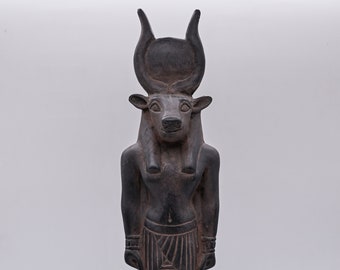 May include: Black statue of the Egyptian god Apis, depicted as a bull-headed man with a sun disk and horns on his head. The statue is standing on a rectangular base with hieroglyphs.