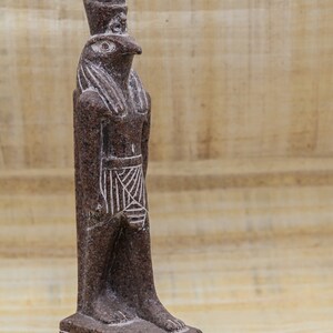 Puede incluir: Una estatua de granito marr&oacute;n del dios egipcio Horus, representado como un hombre con cabeza de halc&oacute;n con una corona alta. La estatua est&aacute; de pie sobre una base rectangular con jerogl&iacute;ficos.