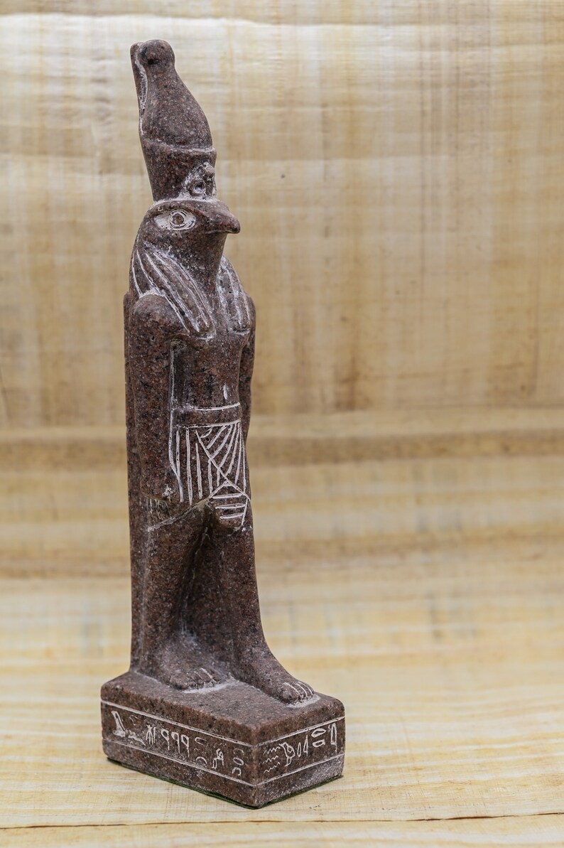 Puede incluir: Una estatua de granito marr&oacute;n del dios egipcio Horus, representado como un hombre con cabeza de halc&oacute;n con una corona alta. La estatua est&aacute; de pie sobre una base rectangular con jerogl&iacute;ficos.
