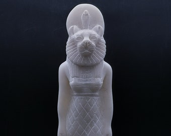 May include: White alabaster statue of the Egyptian goddess Bastet, depicted as a woman with a cat's head. The statue is wearing a traditional Egyptian headdress and a long, flowing robe.