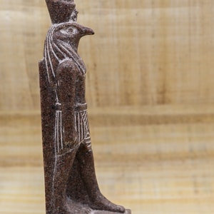 Puede incluir: Una estatua de granito marr&oacute;n del dios egipcio Horus, representado como un hombre con cabeza de halc&oacute;n. La estatua est&aacute; de pie sobre una base con jerogl&iacute;ficos que dicen "Horus, el Grande".