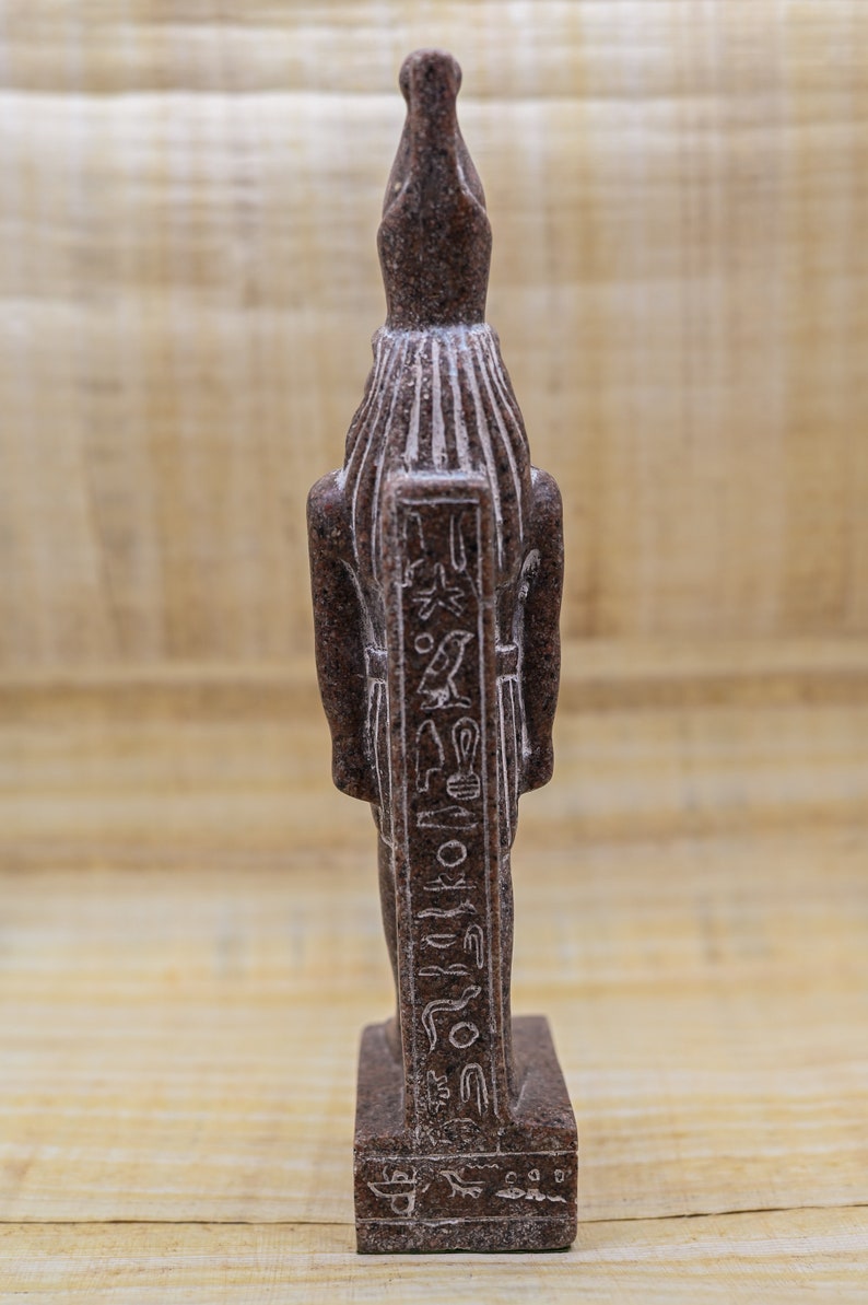 Puede incluir: Una peque&ntilde;a estatua de piedra marr&oacute;n de un dios egipcio con jerogl&iacute;ficos tallados en la parte delantera. La estatua est&aacute; de pie sobre una peque&ntilde;a base.