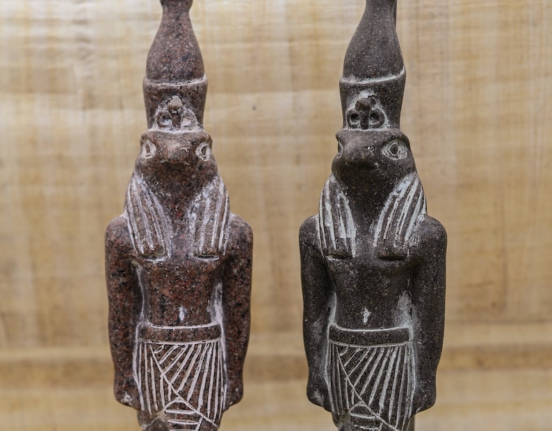 Puede incluir: Dos peque&ntilde;as estatuas de color marr&oacute;n oscuro del dios egipcio Anubis, cada una con cabeza de chacal y cuerpo humano. Las estatuas est&aacute;n de pie y tienen una superficie detallada y texturizada.