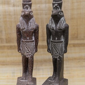 Puede incluir: Dos peque&ntilde;as estatuas de color marr&oacute;n oscuro del dios egipcio Thot, cada una con un tocado y una cabeza de rana. Las estatuas est&aacute;n de pie sobre bases rectangulares con jerogl&iacute;ficos.