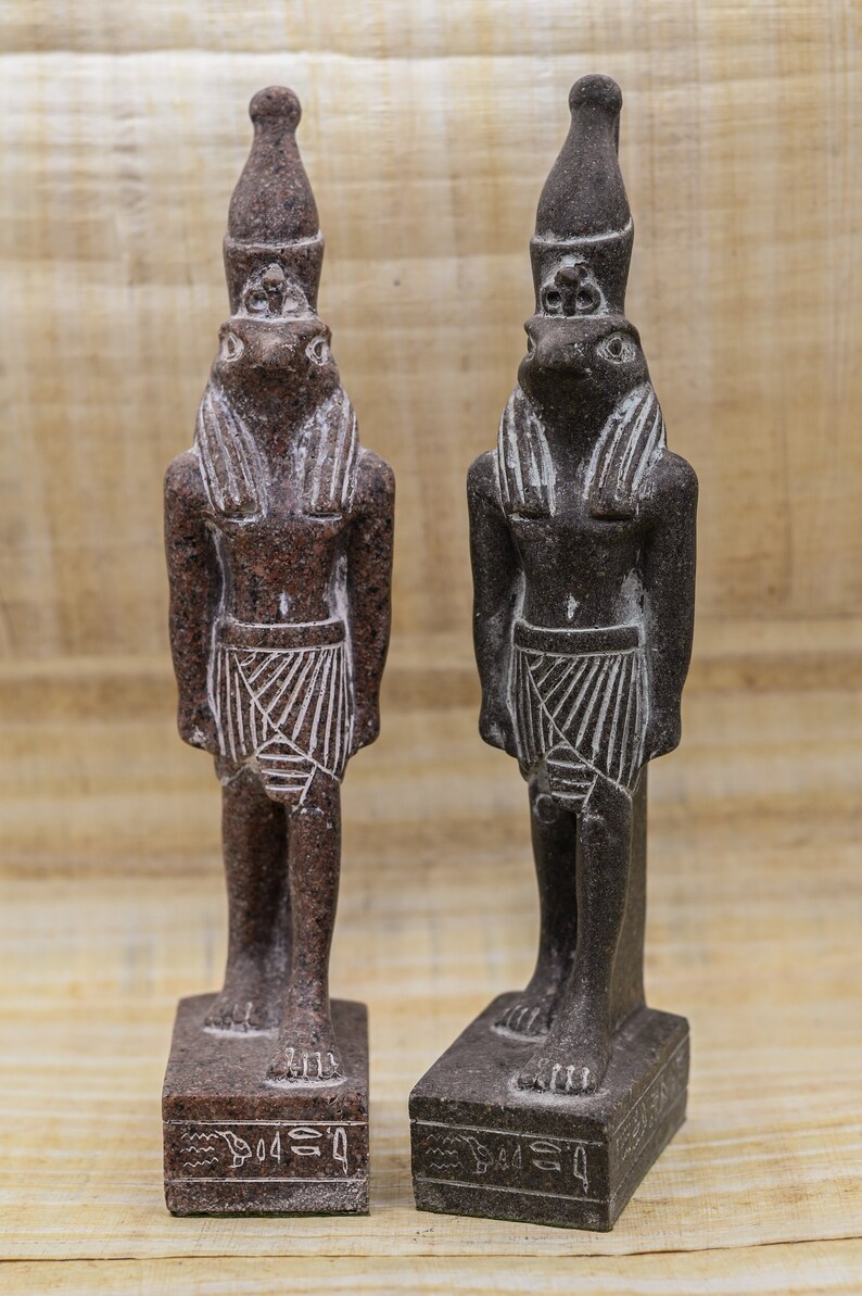 Puede incluir: Dos peque&ntilde;as estatuas de color marr&oacute;n oscuro del dios egipcio Thot, cada una con un tocado y una cabeza de rana. Las estatuas est&aacute;n de pie sobre bases rectangulares con jerogl&iacute;ficos.