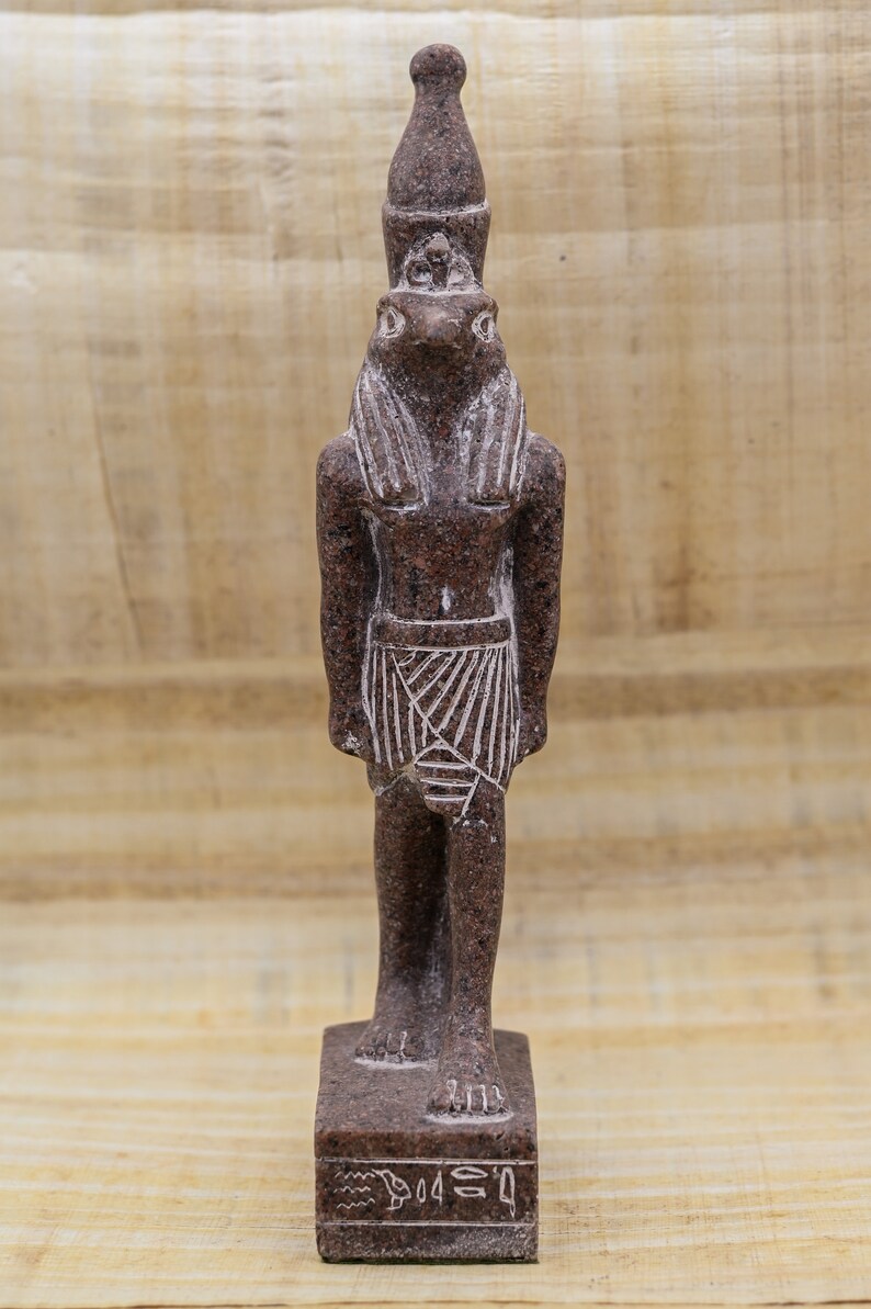 Puede incluir: Una estatua de granito marr&oacute;n del dios egipcio Thot, representado como un humano con la cabeza de un ibis. Lleva un alto tocado puntiagudo y una falda. La estatua est&aacute; de pie sobre una base rectangular con jerogl&iacute;ficos inscritos en ella.
