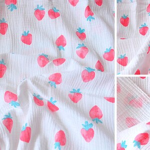 Puede incluir: Tela de muselina blanca con un patr&oacute;n repetido de fresas rosas con hojas azules. La tela es texturizada y tiene un aspecto arrugado.