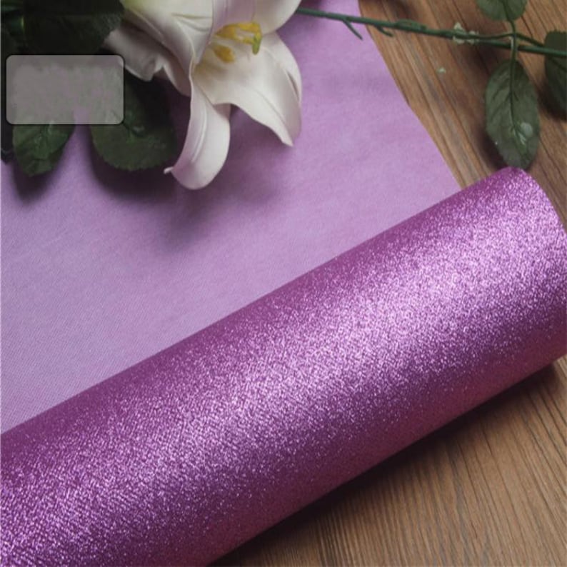 Może przedstawiać: Rolkę purpurowego papieru z brokatem o subtelnym połysku. Papier jest zwinięty i leży na drewnianej powierzchni.