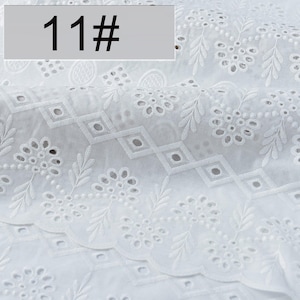 May include: A white fabric featuring intricate eyelet embroidery with floral and leaf motifs, arranged in repeating patterns with diamond-shaped cutouts. A rectangular label with the text 11# is positioned in the upper left corner of the image.