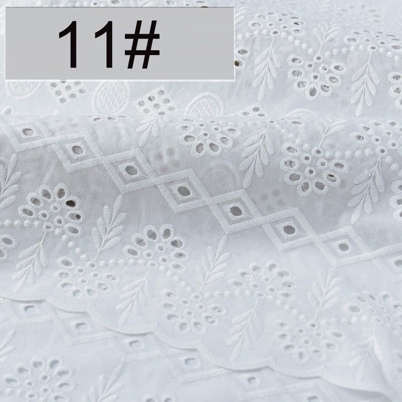 May include: A white fabric featuring intricate eyelet embroidery with floral and leaf motifs, arranged in repeating patterns with diamond-shaped cutouts. A rectangular label with the text 11# is positioned in the upper left corner of the image.