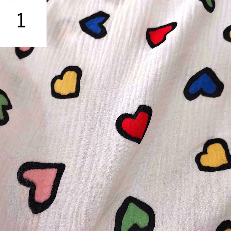 Puede incluir: Tela blanca con un patr&oacute;n repetido de corazones de colores. Los corazones est&aacute;n delineados en negro y rellenos de rojo, azul, verde, amarillo y rosa.