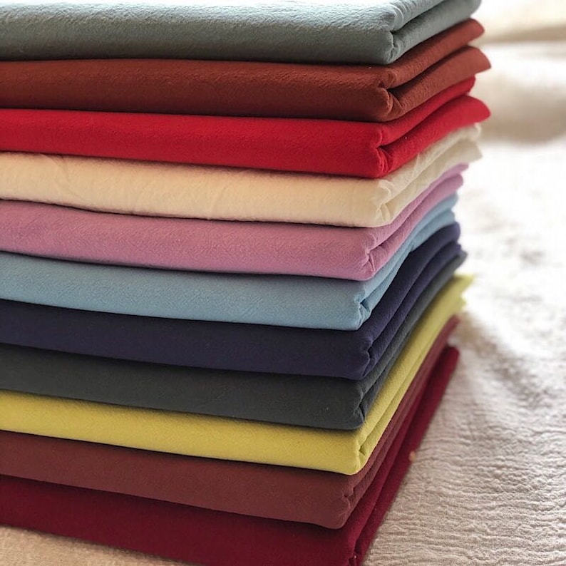 May include: A stack of 12 fabric squares in various colours, including red, blue, green, and purple. The fabric is folded neatly and appears to be a soft, cotton material.
