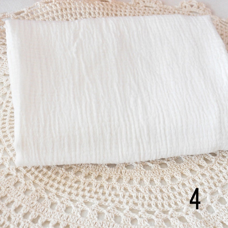 Puede incluir: Tela de algod&oacute;n blanca con una superficie texturizada. La tela est&aacute; doblada y colocada sobre una superficie de crochet. El n&uacute;mero 4 es visible en la esquina inferior derecha de la imagen.