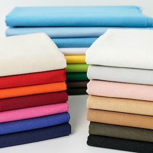 May include: A collection of folded fabric in a variety of colours, including blue, white, red, orange, pink, and brown. The fabric appears to be a medium weight cotton or linen, suitable for sewing projects. The image showcases a range of hues, from light pastels to vibrant shades.