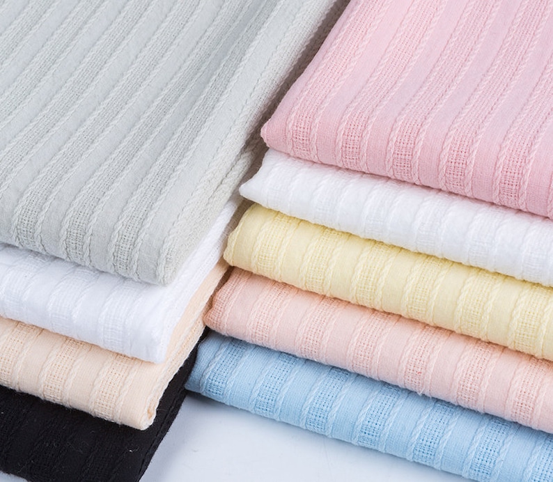 K&ouml;nnte beinhalten: Ein Stapel Stoffmuster in verschiedenen Farben, darunter Grau, Rosa, Wei&szlig;, Gelb, Pfirsich, Blau und Schwarz. Der Stoff hat eine strukturierte, gerippte Oberfl&auml;che.