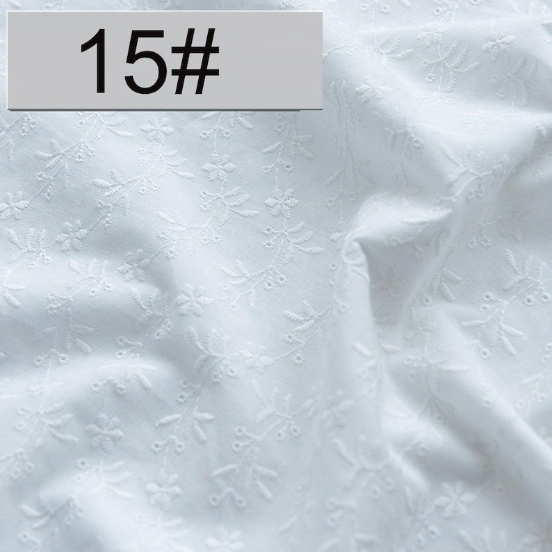 May include: A white fabric featuring a delicate, tonal embroidered floral and vine pattern throughout the material. A rectangular gray label with the black text 15# is positioned in the upper left corner of the image, overlaying the fabric.