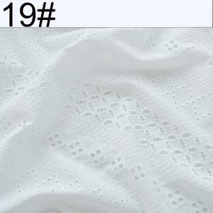 May include: A white fabric featuring intricate eyelet embroidery with repeating geometric patterns and floral-like cutouts. The textile displays a textured surface with visible stitching and openwork details. The text 19# is visible in the top left corner.