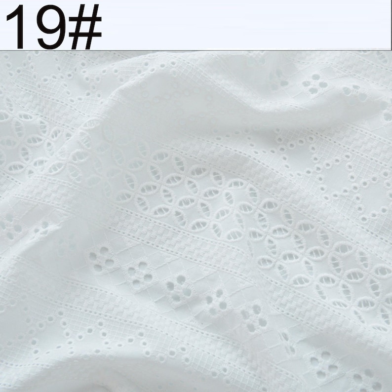 May include: A white fabric featuring intricate eyelet embroidery with repeating geometric patterns and floral-like cutouts. The textile displays a textured surface with visible stitching and openwork details. The text 19# is visible in the top left corner.
