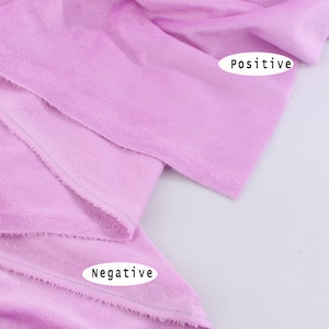 May include: Close-up of a soft, light purple fabric with a slightly textured surface. The fabric is folded over, showing the edges of the fabric. The words "Positive" and "Negative" are written on the fabric.