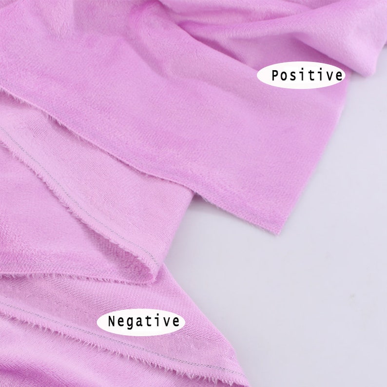 May include: Close-up of a soft, light purple fabric with a slightly textured surface. The fabric is folded over, showing the edges of the fabric. The words "Positive" and "Negative" are written on the fabric.