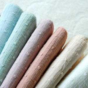Op de afbeelding: Een verzameling van acht stofstalen in verschillende tinten blauw, roze en wit. De stoffen hebben een textuur, een licht bobbelig oppervlak.