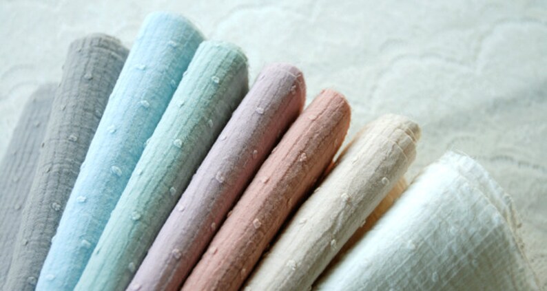 Op de afbeelding: Een verzameling van acht stofstalen in verschillende tinten blauw, roze en wit. De stoffen hebben een textuur, een licht bobbelig oppervlak.