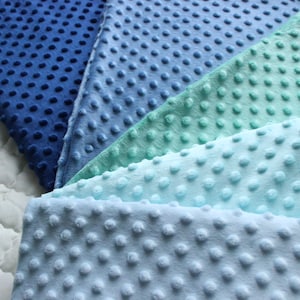 Op de afbeelding: Een stapel van vijf stofstalen in verschillende tinten blauw en groen. De stof heeft een textuur met stippen.