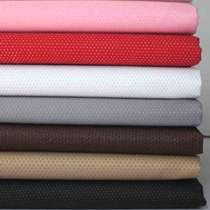 May include: A stack of six fabric swatches in various colors, including pink, red, white, gray, brown, beige, and black. Each swatch has a textured surface with small, evenly spaced dots.