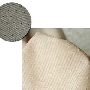 Op de afbeelding: Close-up van een beige stof met een textuurpatroon van kleine stippen en horizontale lijnen.