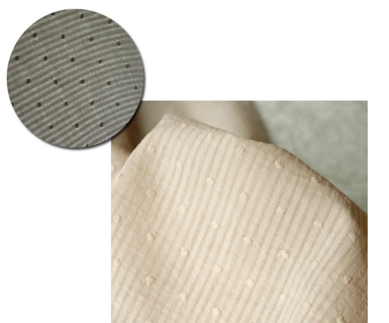 Op de afbeelding: Close-up van een beige stof met een textuurpatroon van kleine stippen en horizontale lijnen.