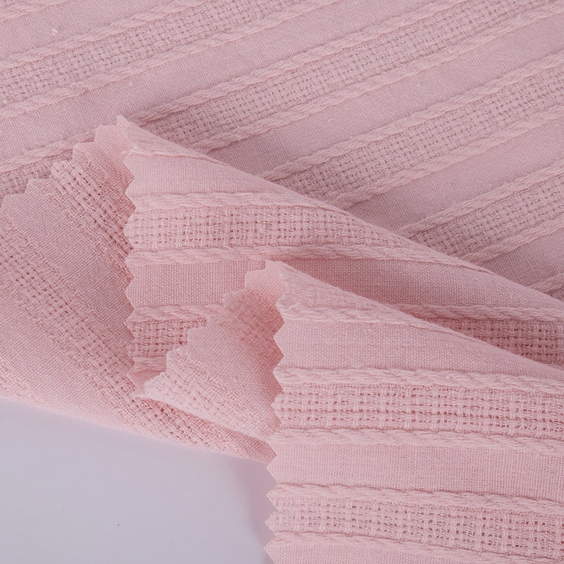 K&ouml;nnte beinhalten: Nahaufnahme eines rosa Stoffes mit einem strukturierten, gestreiften Muster. Der Stoff ist weich und hat eine leicht zerknitterte Optik.