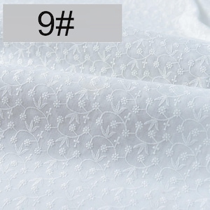 May include: A white fabric featuring an intricate, repeating embroidered pattern of small flowers and delicate leaves. The textile has a soft, folded texture and includes a rectangular overlay in the top left corner displaying the text 9#.
