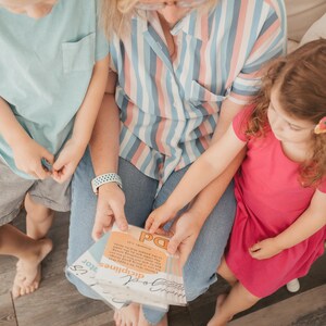 May include: A woman sits with two children, reading a book with the title "Encouraging Disciplines" and the text "For the purpose of the law is love, which grows out of a pure heart and a good conscience and a sincere faith."